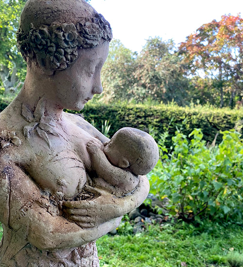 En trädgårdsstaty av en kvinna som ammar ett barn.